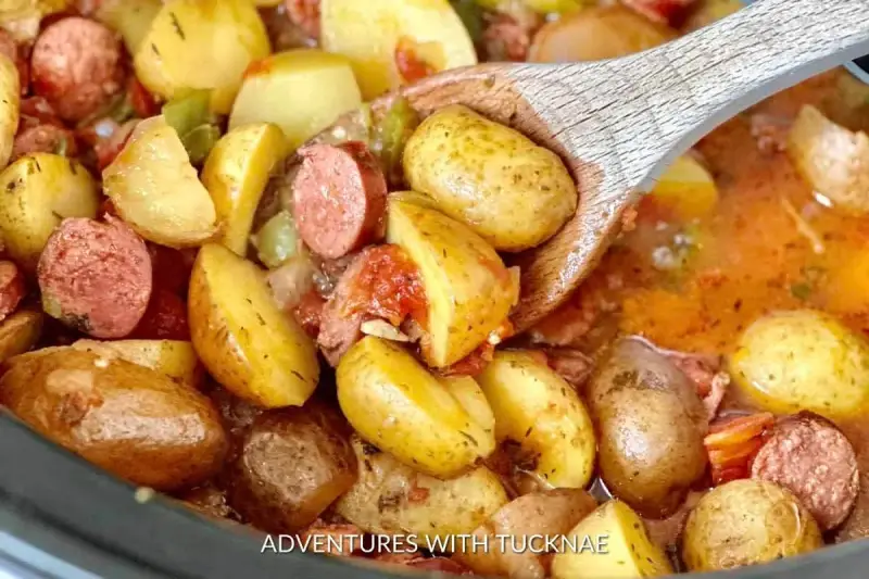 A wooden spoon scoops up hearty potatoes and sausage from a crockpot, perfect for camping crockpot meals.