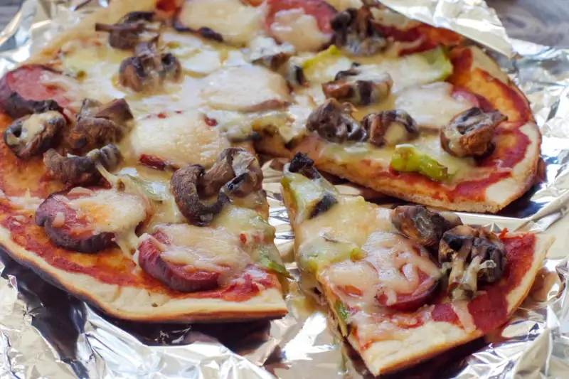 Delicious grilled pizza ideas: a pizza with mushrooms, sausage, and melted cheese on foil.